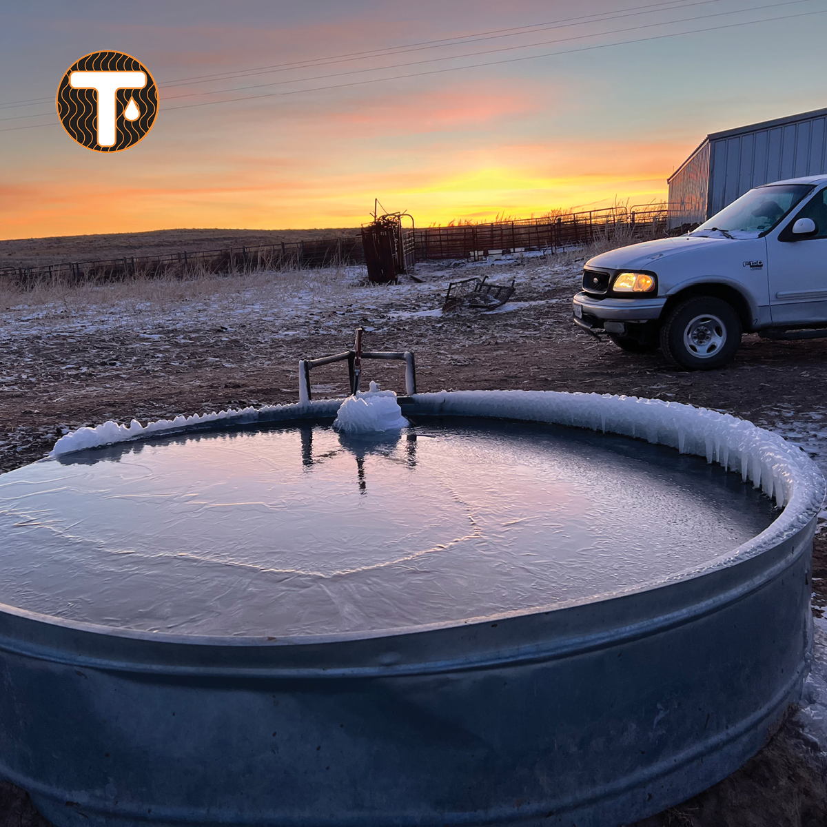 Frozen water tank on a farm with a sunset sky and a white truck in the background.